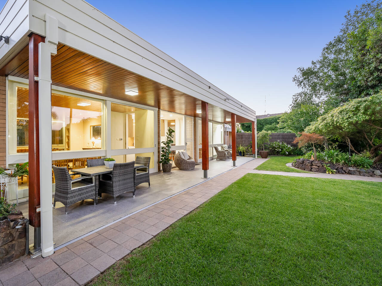 A covered outdoor dining area beside a lawn at dusk